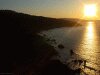 Dark toned photo of sun setting on hilly ocean shore (west coast)