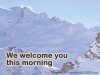 Full screen photo of snow covered mountain against a light sky, low contrast with text 'we welcome you this morning'