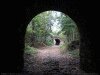 color photo of road as seen through silhouetted mouth of tunnel, direction.
